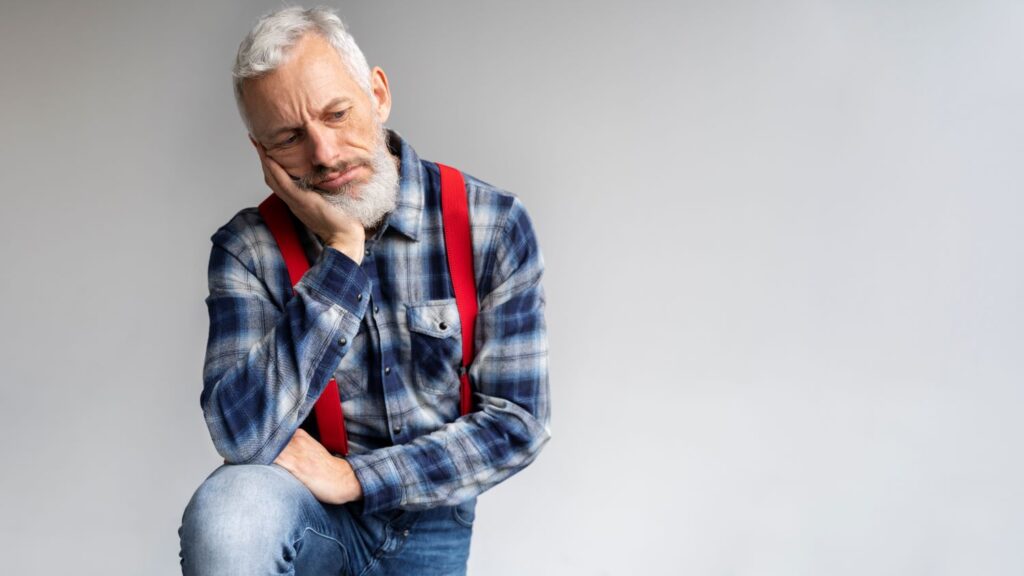 Com uma mão no queixo, homem mais velho pensa se está com próstata aumentada ou câncer