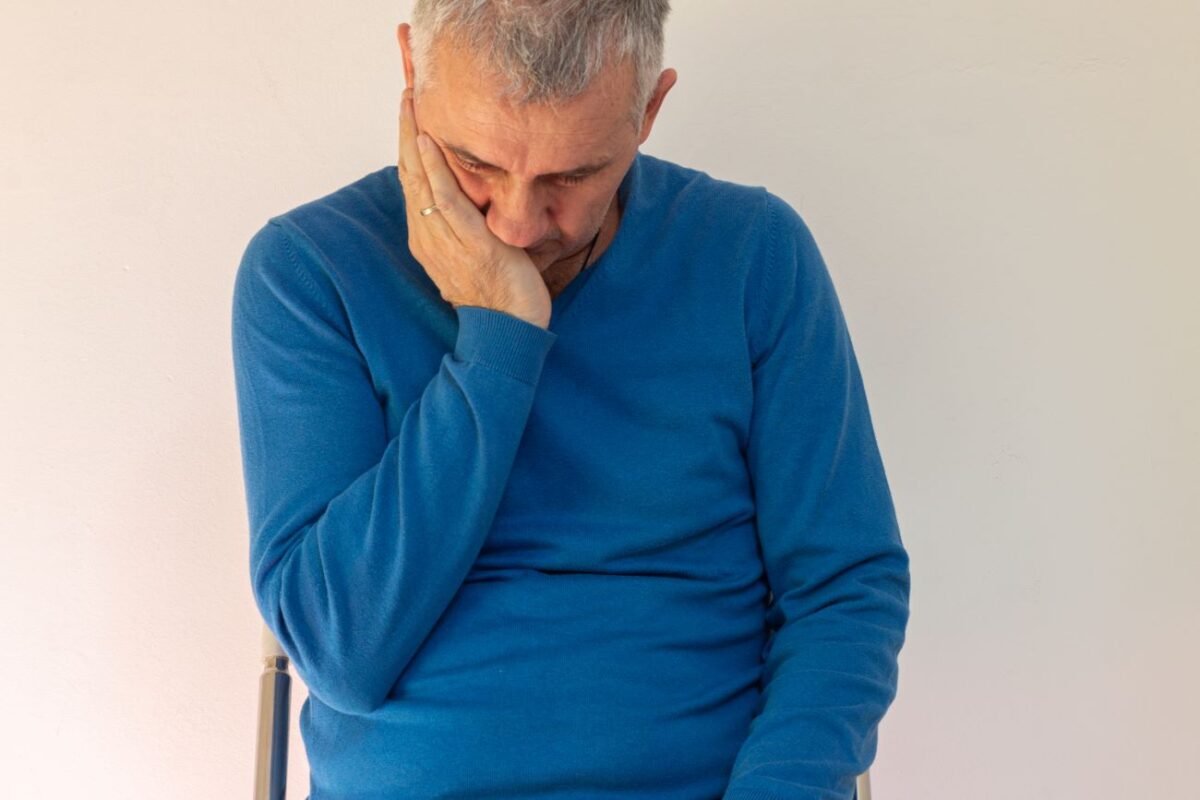 Homem com expressão de desconforto coloca a mão no rosto devido à próstata inchada