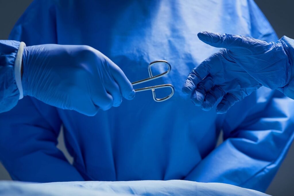 Médicos enluvados seguram pinça durante cirurgia do câncer de próstata