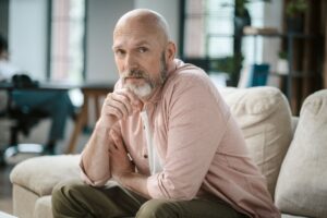 Homem de meia-idade sentado em um sofá com expressão pensativa e olhar atento, refletindo sobre diagnóstico e prognóstico de câncer de próstata avançado, incluindo a questão: “Gleason 10 tem cura?”.
