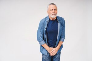 Homem idoso com expressão de desconforto segurando a região pélvica, ilustrando a dúvida sobre se a cirurgia de próstata causa incontinência urinária e seus possíveis impactos na qualidade de vida.