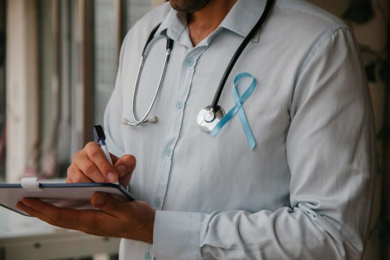 Médico com estetoscópio e laço azul fazendo anotações, ilustrando o estadiamento do câncer de próstata e a avaliação da extensão da doença.
